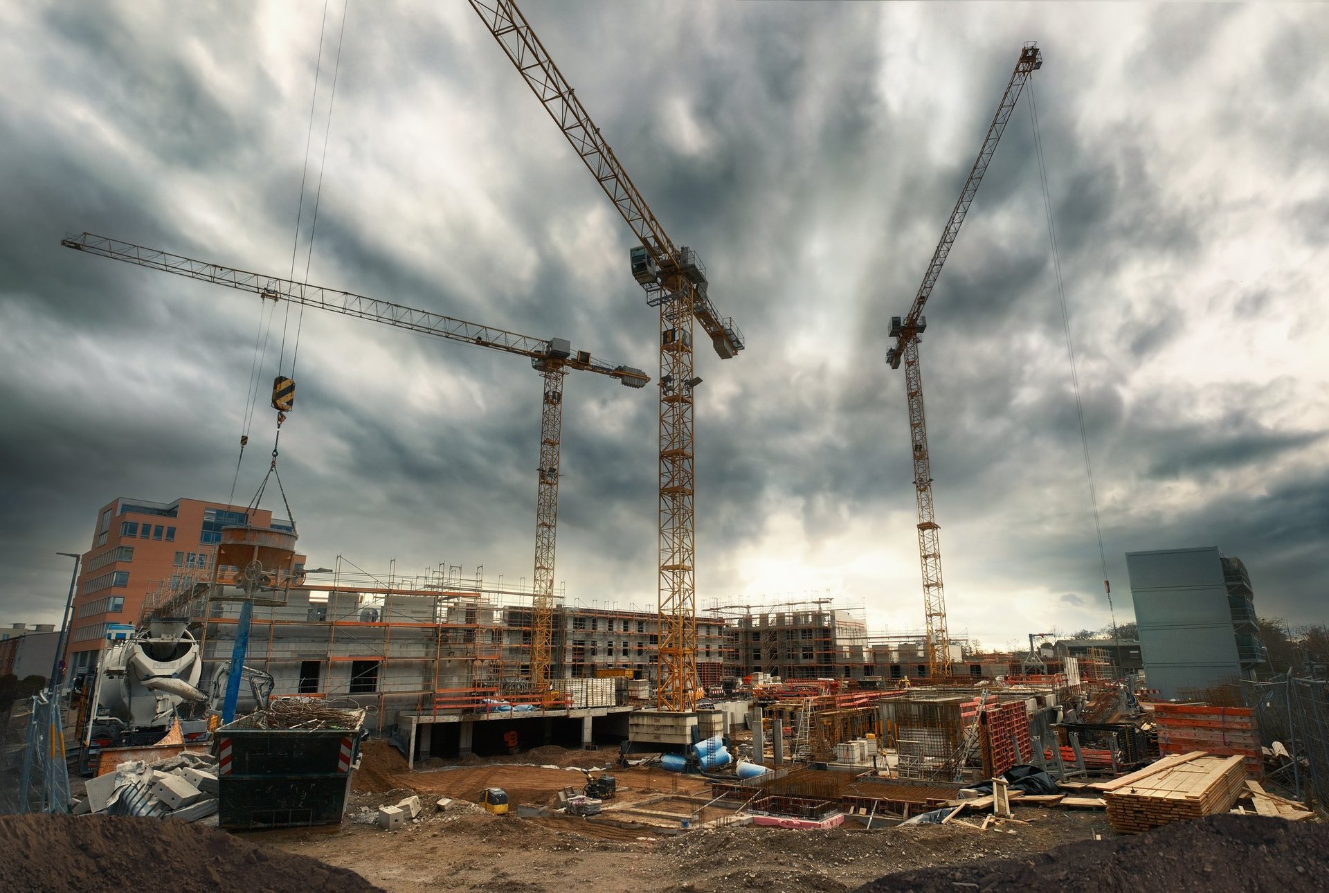 Construction site with cranes looming into the dramatic cloudy sky