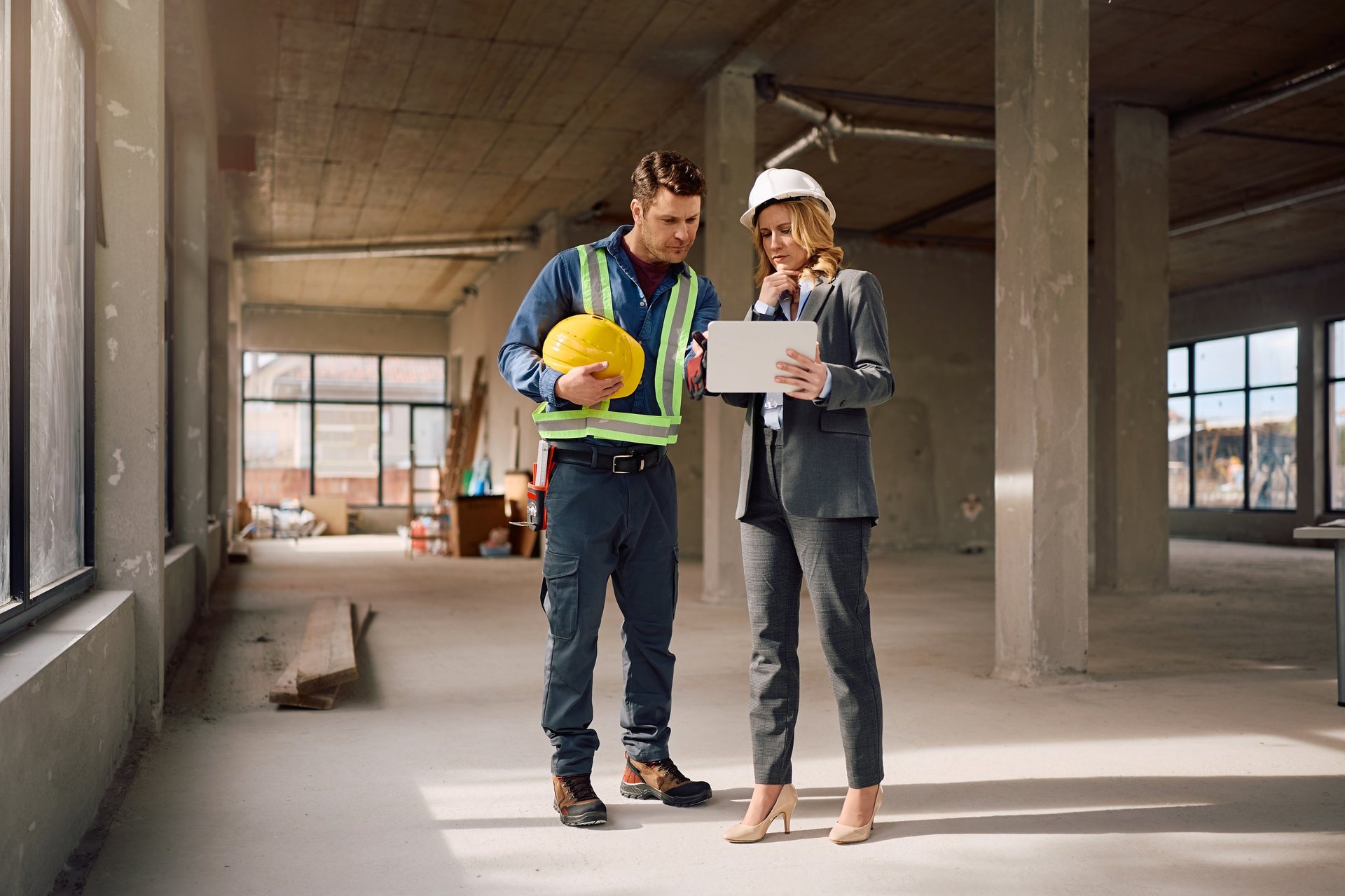 Female architect and manual worker going through housing plans on touchpad at construction site